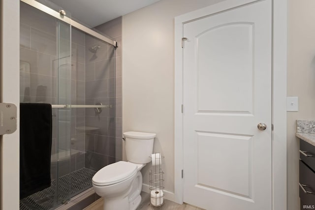 bathroom featuring vanity, a stall shower, toilet, and baseboards