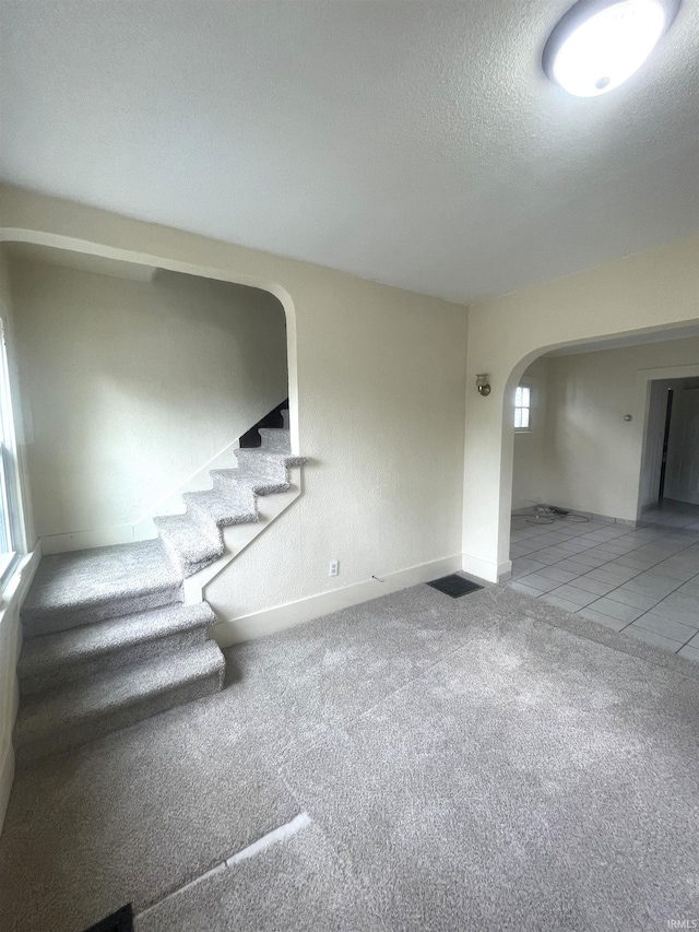 1307 High St, Logansport, IN 46947 - unfurnished living room featuring arched walkways, a textured ceiling, stairway, carpet, and baseboards