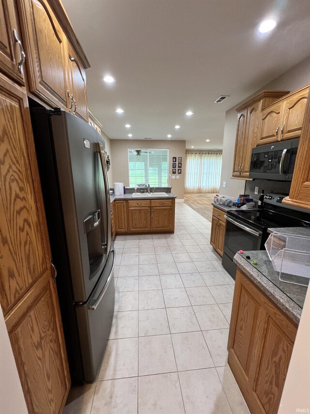 1155 N Fox Ridge Links Dr, Vincennes, IN 47591 - kitchen with black refrigerator with ice dispenser, electric stove, a sink, brown cabinetry, and light tile patterned flooring