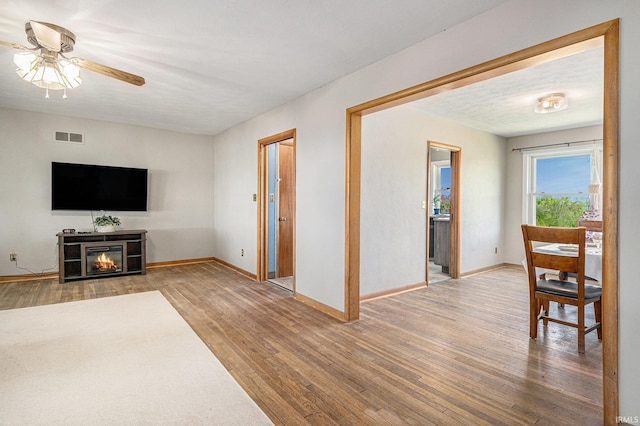 living area with wood finished floors, a ceiling fan, baseboards, and a glass covered fireplace