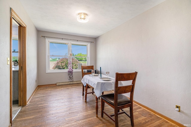 dining space featuring a baseboard radiator, hardwood / wood-style flooring, and baseboards