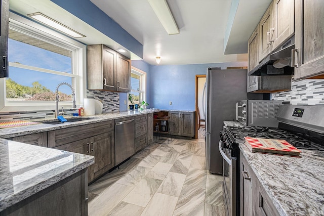 kitchen with appliances with stainless steel finishes, a sink, under cabinet range hood, and tasteful backsplash