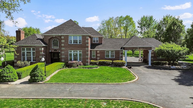 view of front of property featuring a front lawn, a chimney, brick siding, driveway, and an attached carport