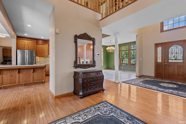 entrance foyer featuring light wood finished floors, a chandelier, decorative columns, baseboards, and a high ceiling