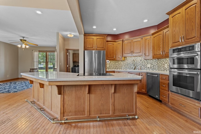 kitchen featuring appliances with stainless steel finishes, light wood finished floors, a sink, a kitchen breakfast bar, and recessed lighting