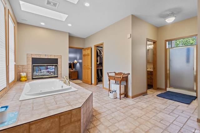 full bath with a jetted tub, a skylight, a tiled fireplace, a spacious closet, and recessed lighting