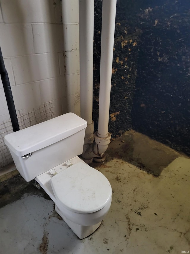 bathroom with toilet and concrete block wall