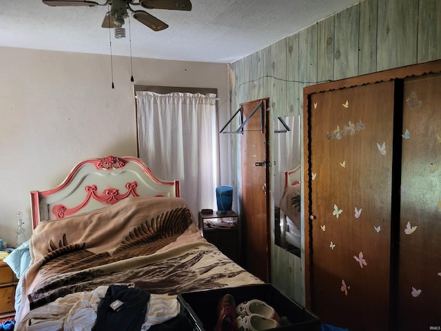 bedroom with a textured ceiling, wooden walls, and a ceiling fan