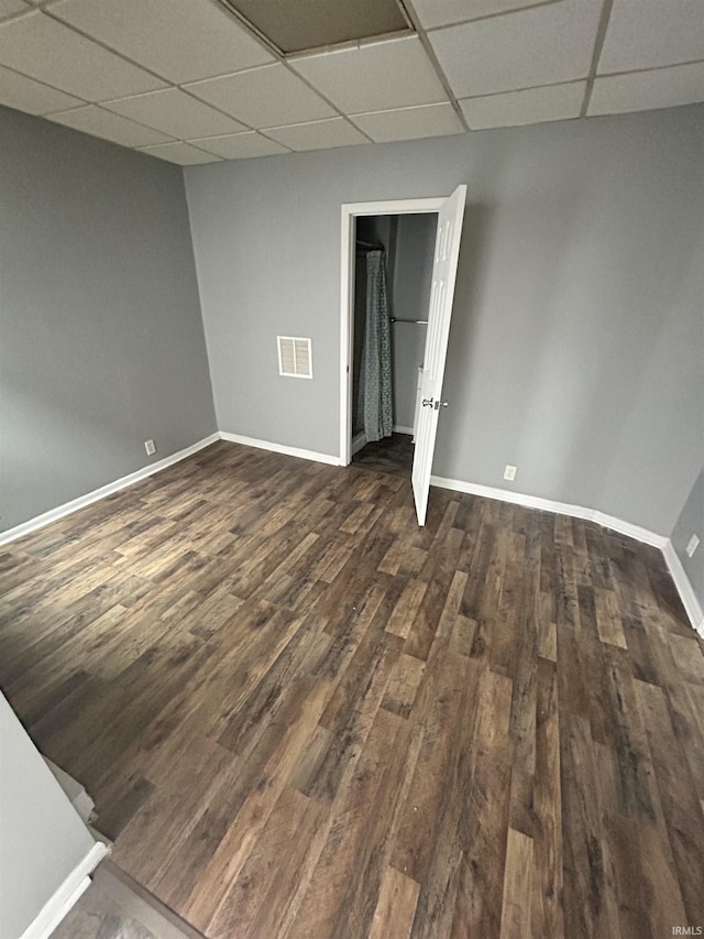 unfurnished room with a drop ceiling, dark wood-style floors, and baseboards