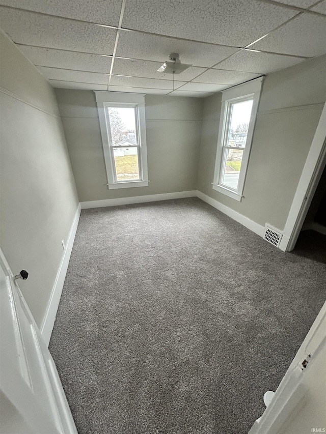 empty room featuring carpet flooring, a paneled ceiling, and baseboards
