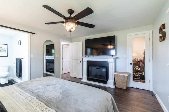 bedroom with a glass covered fireplace, dark wood finished floors, baseboards, a ceiling fan, and arched walkways