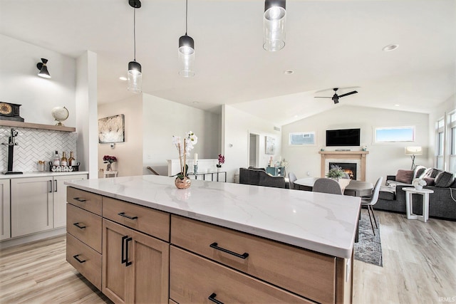 kitchen with light wood-style flooring, a warm lit fireplace, open floor plan, tasteful backsplash, and vaulted ceiling