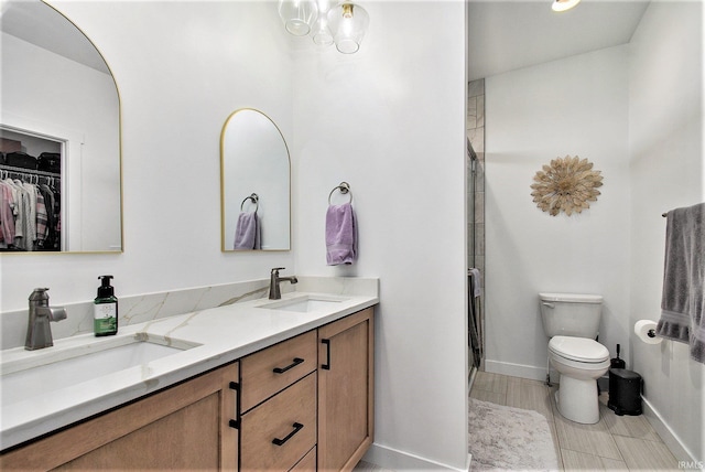 bathroom with double vanity, baseboards, toilet, a shower with door, and a walk in closet