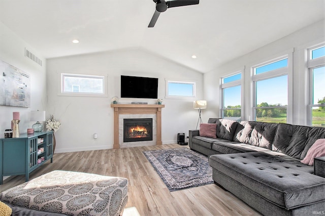 living area featuring light wood-style floors, lofted ceiling, ceiling fan, a tile fireplace, and baseboards