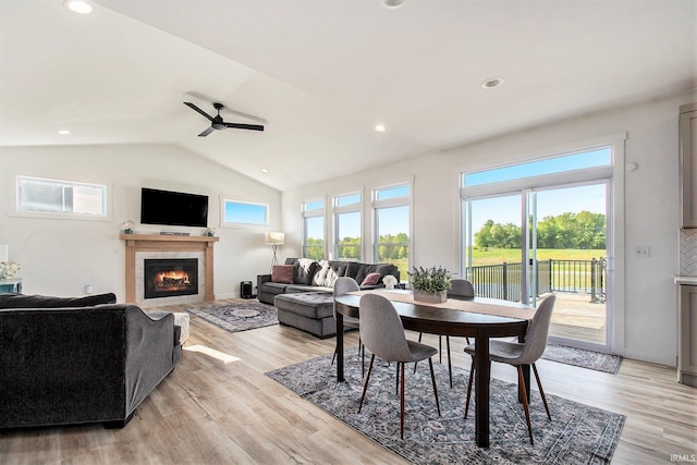 dining area with a tile fireplace, plenty of natural light, lofted ceiling, light wood-style flooring, and ceiling fan