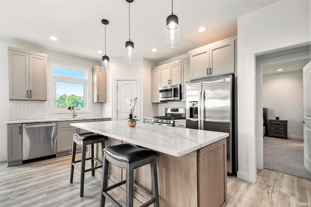 kitchen with appliances with stainless steel finishes, a kitchen island, light stone counters, tasteful backsplash, and light wood-style flooring