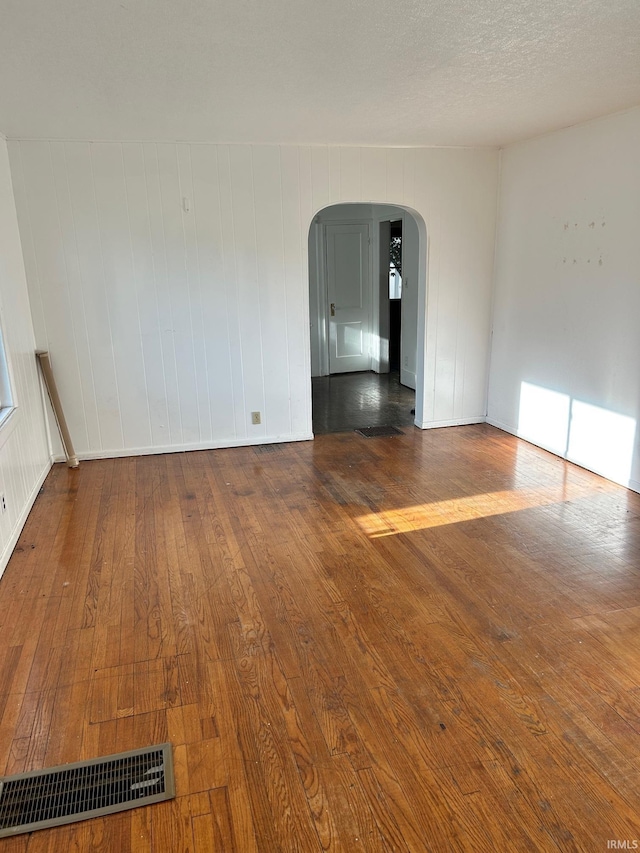 spare room with arched walkways, wood finished floors, and baseboards