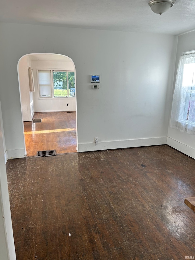 spare room featuring arched walkways, hardwood / wood-style flooring, healthy amount of natural light, and baseboards