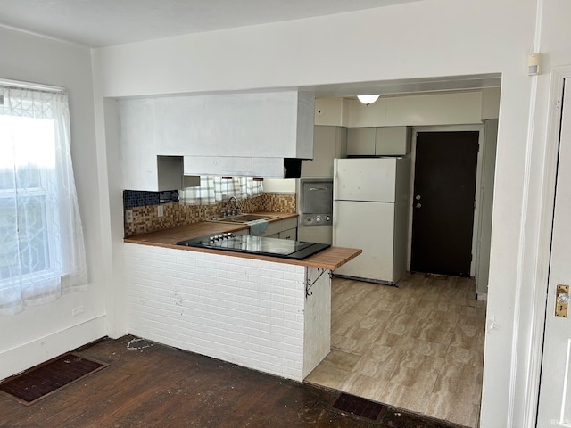 kitchen featuring freestanding refrigerator, black electric cooktop, wood finished floors, decorative backsplash, and a sink