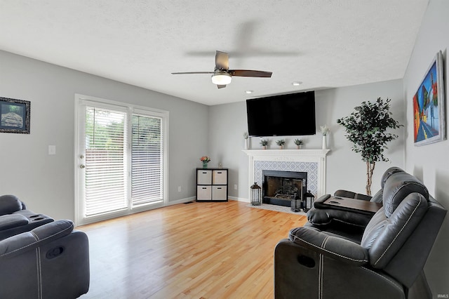 4113 S Hedgewood Ct, Bloomington, IN 47403 - living room with a ceiling fan, light wood-style floors, a tiled fireplace, a textured ceiling, and baseboards