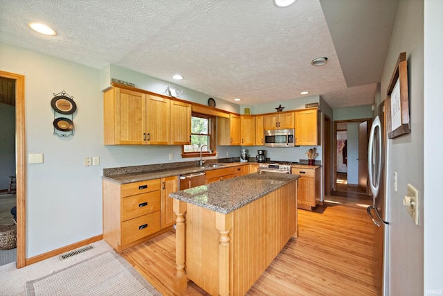 kitchen with stainless steel appliances, light wood finished floors, a center island, a sink, and dark stone countertops