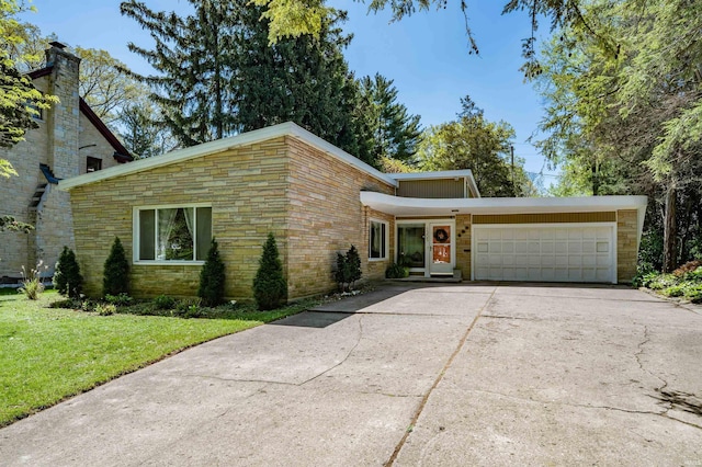 mid-century home with concrete driveway, stone siding, an attached garage, and a front lawn