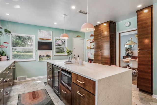 kitchen featuring stainless steel microwave, beverage cooler, baseboards, decorative light fixtures, and a kitchen island