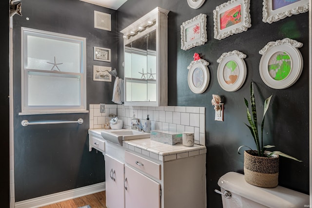 bathroom with decorative backsplash, wood finished floors, toilet, and vanity