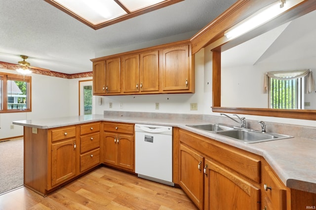 kitchen featuring white dishwasher, a sink, a peninsula, light wood-style flooring, and light countertops