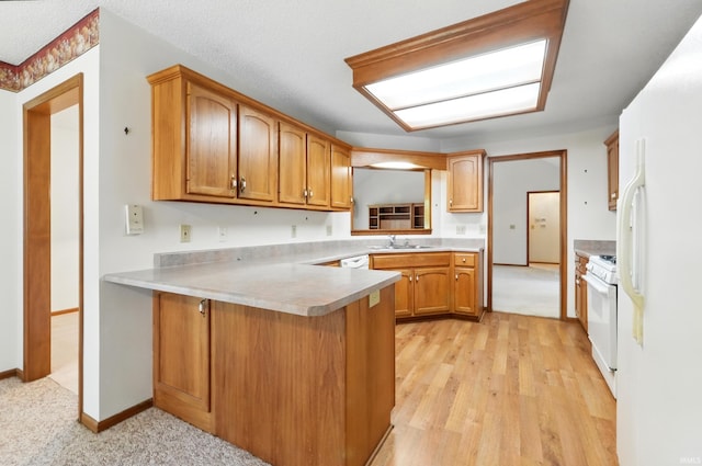 kitchen with a sink, white appliances, a peninsula, brown cabinetry, and light countertops