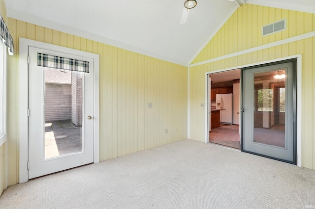 empty room with carpet floors, lofted ceiling, healthy amount of natural light, and wood walls