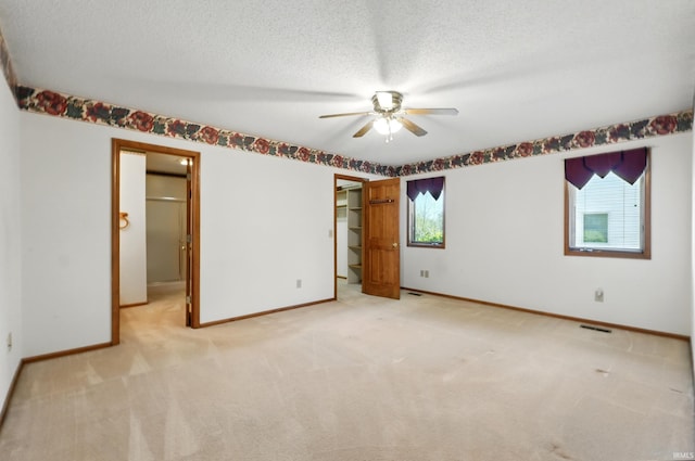 unfurnished bedroom with a walk in closet, light colored carpet, baseboards, and a textured ceiling