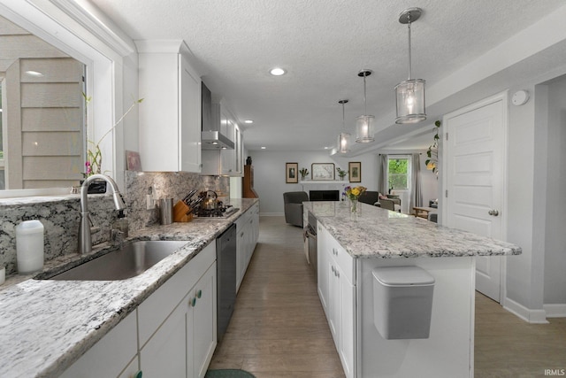 kitchen with a sink, appliances with stainless steel finishes, open floor plan, wall chimney range hood, and decorative backsplash