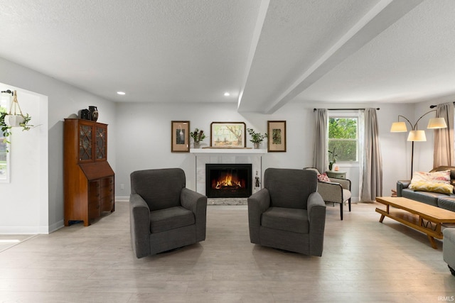living area with a tiled fireplace, recessed lighting, baseboards, light wood-type flooring, and a textured ceiling