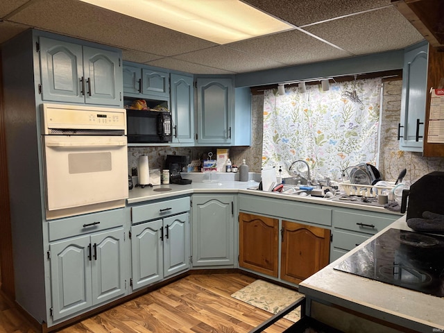 909 N Sullivan St, Alexandria, IN 46001 - kitchen with oven, a drop ceiling, black microwave, a sink, and light wood-style floors