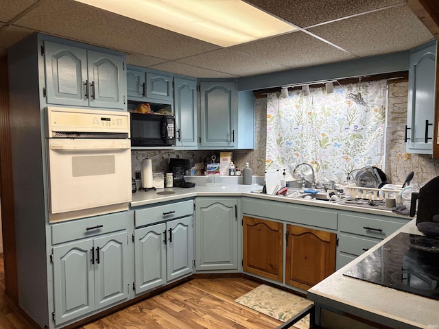 909 N Sullivan St, Alexandria, IN 46001 - kitchen with oven, a paneled ceiling, black microwave, light wood-style flooring, and a sink