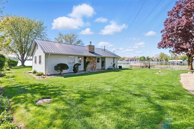 rear view of property featuring a lawn, metal roof, a water view, and a chimney
