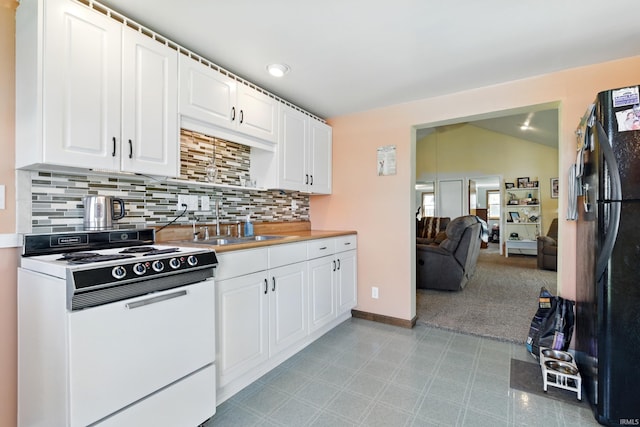 kitchen with electric stove, a sink, backsplash, freestanding refrigerator, and white cabinetry