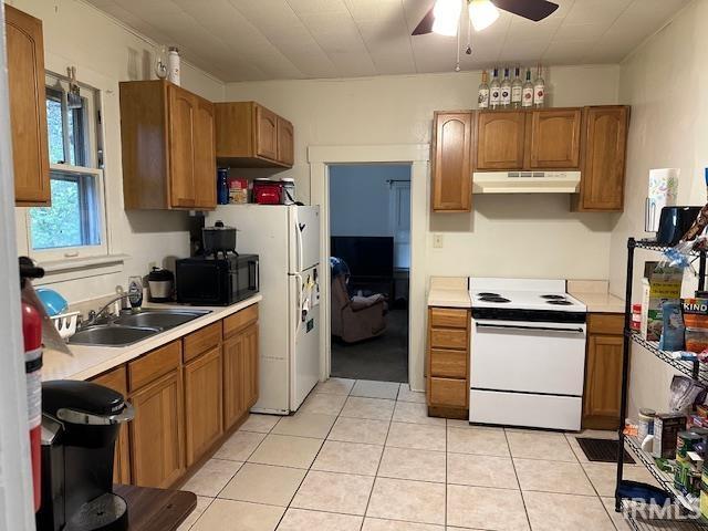 kitchen with white appliances, a sink, under cabinet range hood, and light countertops