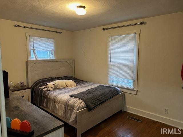 bedroom with multiple windows, dark wood-style floors, and baseboards