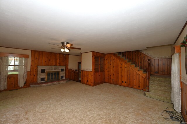unfurnished living room with wooden walls, a ceiling fan, light colored carpet, stairway, and a fireplace