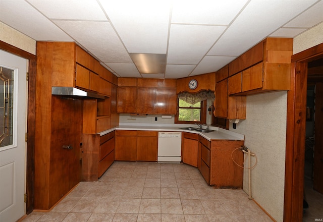 kitchen with brown cabinets, white dishwasher, a sink, under cabinet range hood, and light countertops
