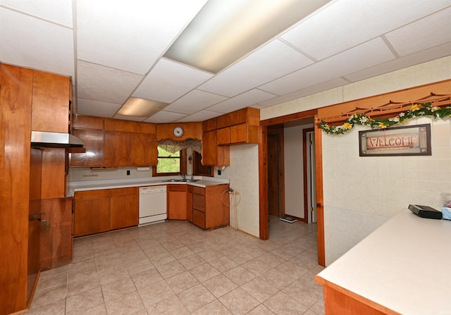 kitchen featuring dishwasher, brown cabinetry, a sink, light countertops, and a paneled ceiling