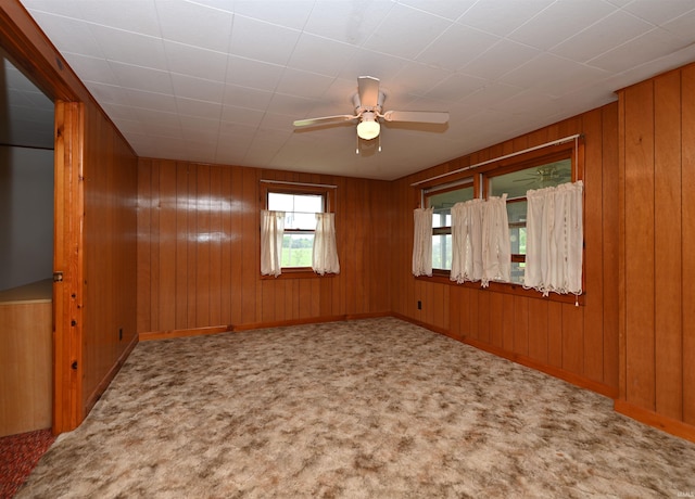 carpeted spare room featuring a ceiling fan, wooden walls, and baseboards