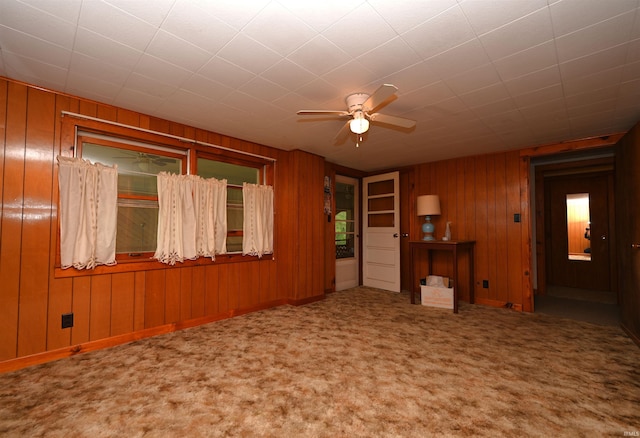 unfurnished living room featuring a ceiling fan, wooden walls, and carpet flooring
