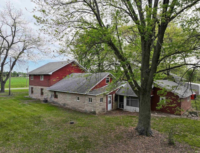 view of side of property with stone siding, a sunroom, a yard, and roof with shingles