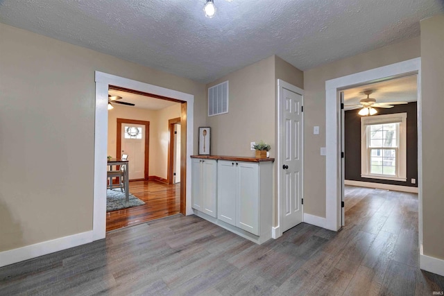 hall with wood finished floors, baseboards, and a textured ceiling
