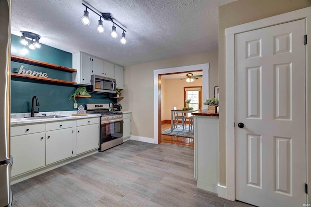 kitchen featuring stainless steel appliances, a sink, a textured ceiling, open shelves, and light wood finished floors