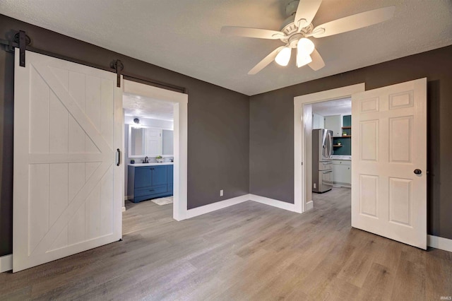 unfurnished room featuring baseboards, light wood-style flooring, a barn door, and ceiling fan
