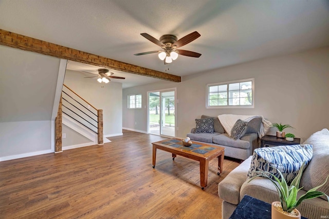 living area featuring stairs, wood finished floors, a ceiling fan, baseboards, and beamed ceiling